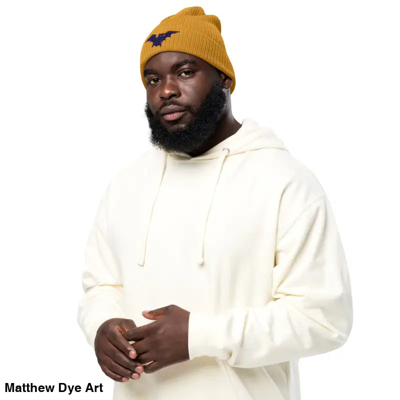 Man in a mustard beanie and cream hoodie showcasing the Bat Baby Beanie for autumn