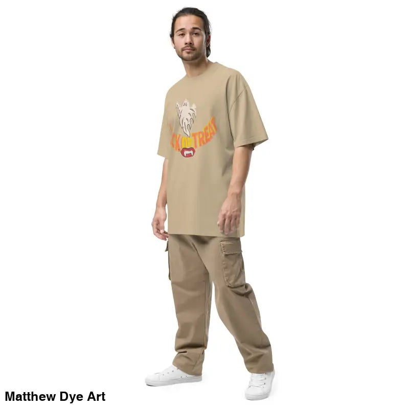 Man in a tan outfit wearing an oversized faded t-shirt featuring vampire fangs design