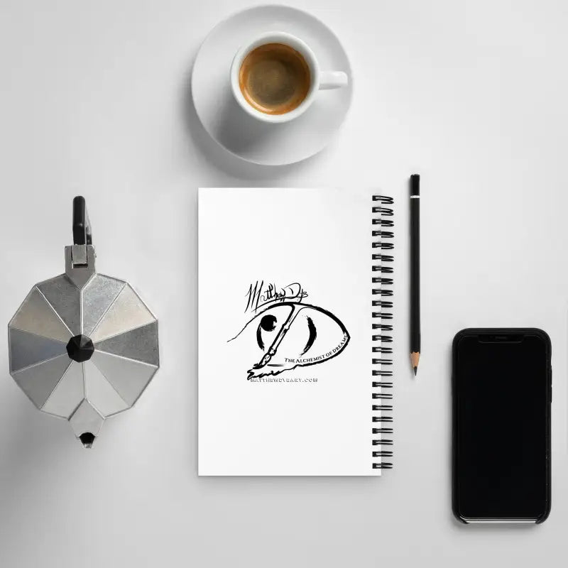 Black and white logo sketch on a notepad with coffee, smartphone, and The Haunting Depths horror spiral notebook