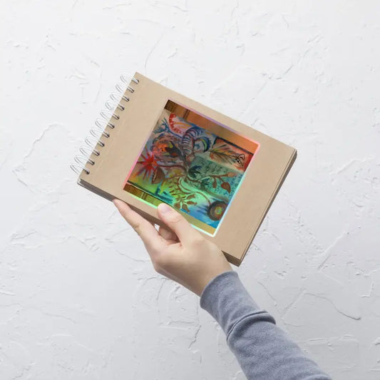 Hand holding an open spiral notebook showcasing colorful artwork and holographic stickers